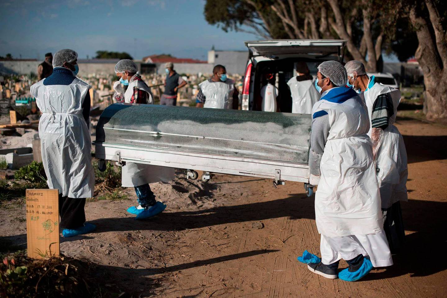 TOPSHOT - Members of a family dressed in personal protective equipment (PPE) carry the casket containing the body of a man who died of COVID-19 coronavirus for a Muslim burial at the Klip Road Cemetry in Grassy Park, Cape Town, on June 9, 2020. - The 54 year old school taxi driver died earlier in the day. (Photo by RODGER BOSCH / AFP)