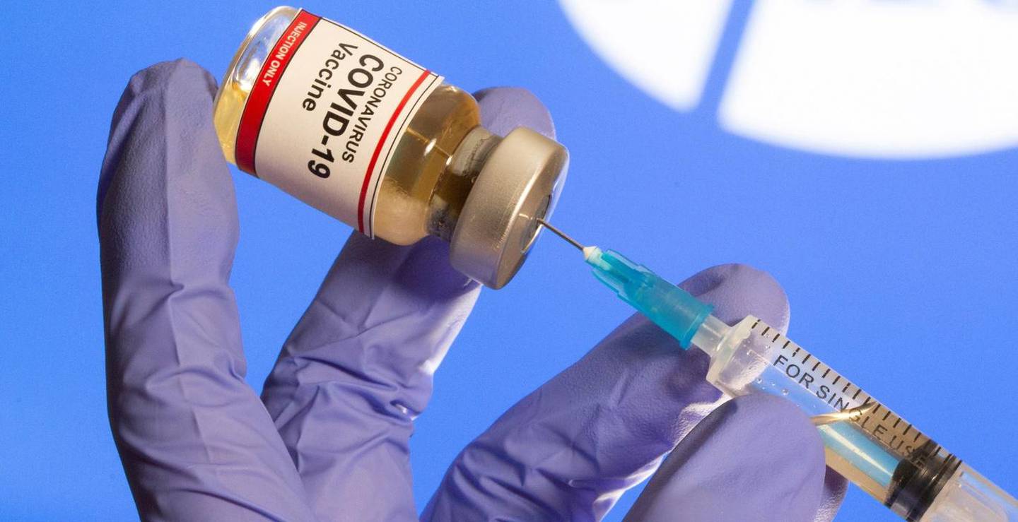 FILE PHOTO: A woman holds a small bottle labeled with a "Coronavirus COVID-19 Vaccine" sticker and a medical syringe in front of displayed Pfizer logo in this illustration taken, October 30, 2020. REUTERS/Dado Ruvic/File Photo