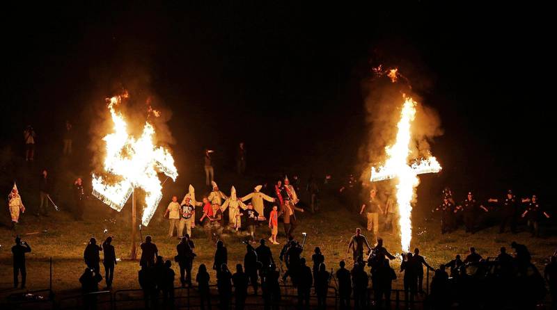 FILE - In this April 23, 2016 file photo, members of the Ku Klux Klan participate in cross and swastika burnings after a "white pride" rally in rural Paulding County near Cedar Town, Ga.  Extremist groups are joining together with a shared goal for whites. A new Ku Klux Klan alliance formed in March 2017 has united chapters from around the country, and a consortium of organizations composed of white nationalists and white separatists is marking its first anniversary. Watchdog groups say white extremists typically can?Äôt work together because of jealousy and infighting. But leaders say they?Äôre united as never before. (AP Photo/Mike Stewart)