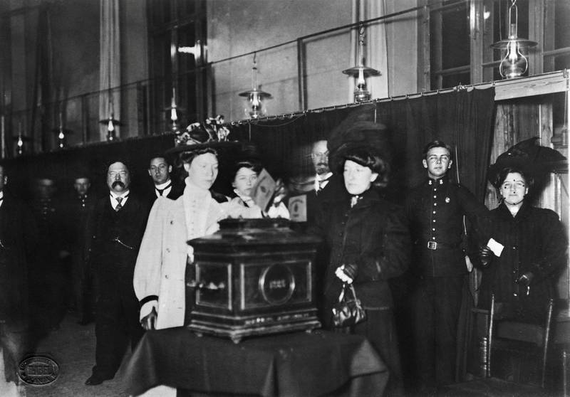 En kvinne legger stemmeseddelen i urnen ved kommunevalget i 1910. Stemmeretten for kvinner i 1901 var begrenset til de med inntekt eller mann som betalte skatt. Først ved kommunevalget i 1910 fikk kvinner stemmerett på lik linje med menn.