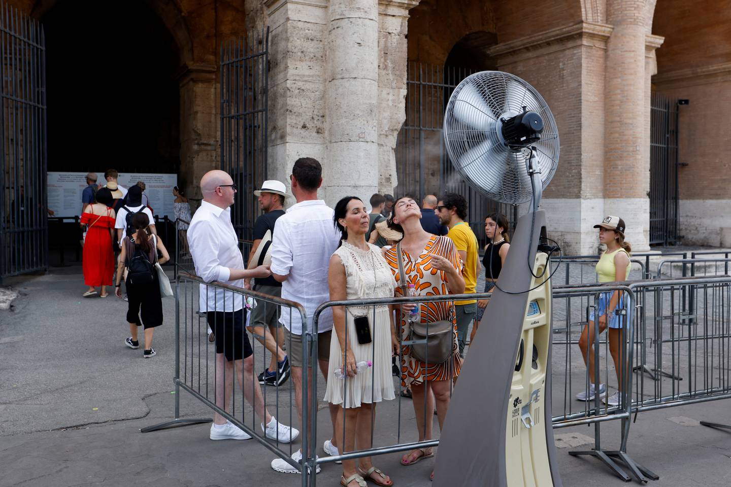 Turister på vei inn i Colosseum kjøler seg ned foran en stor vifte plassert ved køen.
