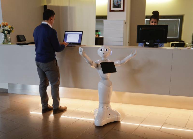 Robot Robby Pepper stands at the front desk of hotel in Peschiera del Garda, northern Italy, Monday, March 12, 2018. Robby Pepper, billed as Italy?Äôs first robot concierge, has been programed to answer simple guest questions in Italian, English and German, the humanoid, speaking robot will be deployed all season at a hotel on the popular Garda Lake to help relieve the desk staff of simple, repetitive questions. Standing at left is Jampaa Innovative digital services product manager Marco Vescovi. (AP Photo/Luca Bruno)