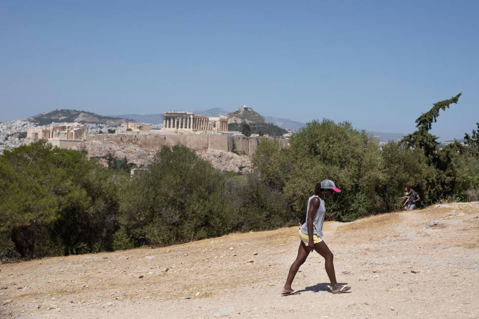 A tourist walks at at Filopappos hill as at the background stands the Acropolis hill with the ancient Parthenon temple during a hot day in Athens, on Thursday, July 4, 2019.  Greece's most famous archaeological site, the Acropolis in Athens, has shut down to visitors for four hours because of hot weather in the capital. (AP Photo/Petros Giannakouris)