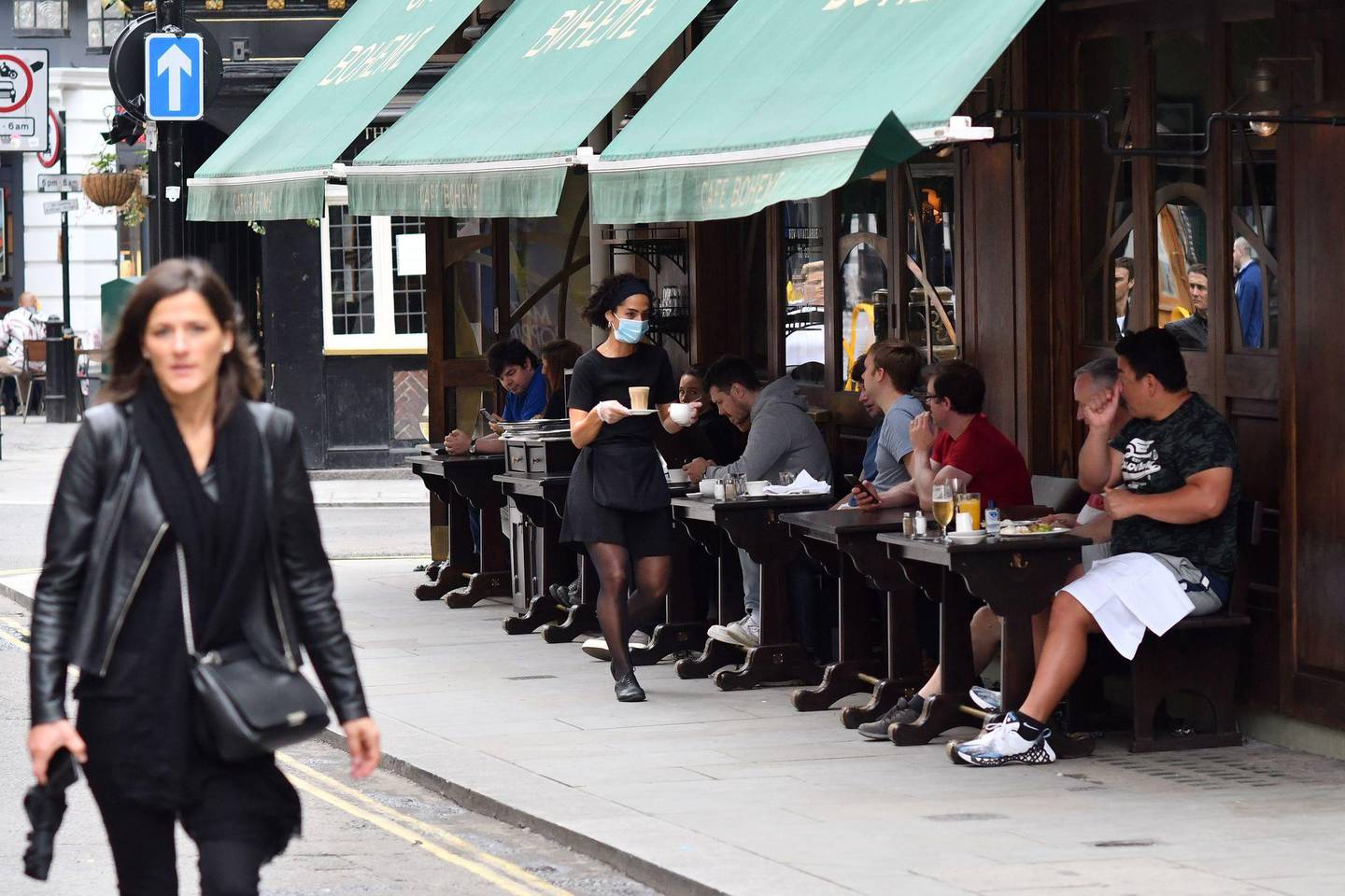 A member of staff wearing a protective face covering serves customers at an outside table at Cafe Boheme in Soho in London on July 4, 2020, as the Soho area embraces pedestrianisation in line with an easing of restrictions during the novel coronavirus COVID-19 pandemic. - Pubs in England reopen on Saturday for the first time since late March, bringing cheer to drinkers and the industry but fears of public disorder and fresh coronavirus cases. (Photo by JUSTIN TALLIS / AFP)