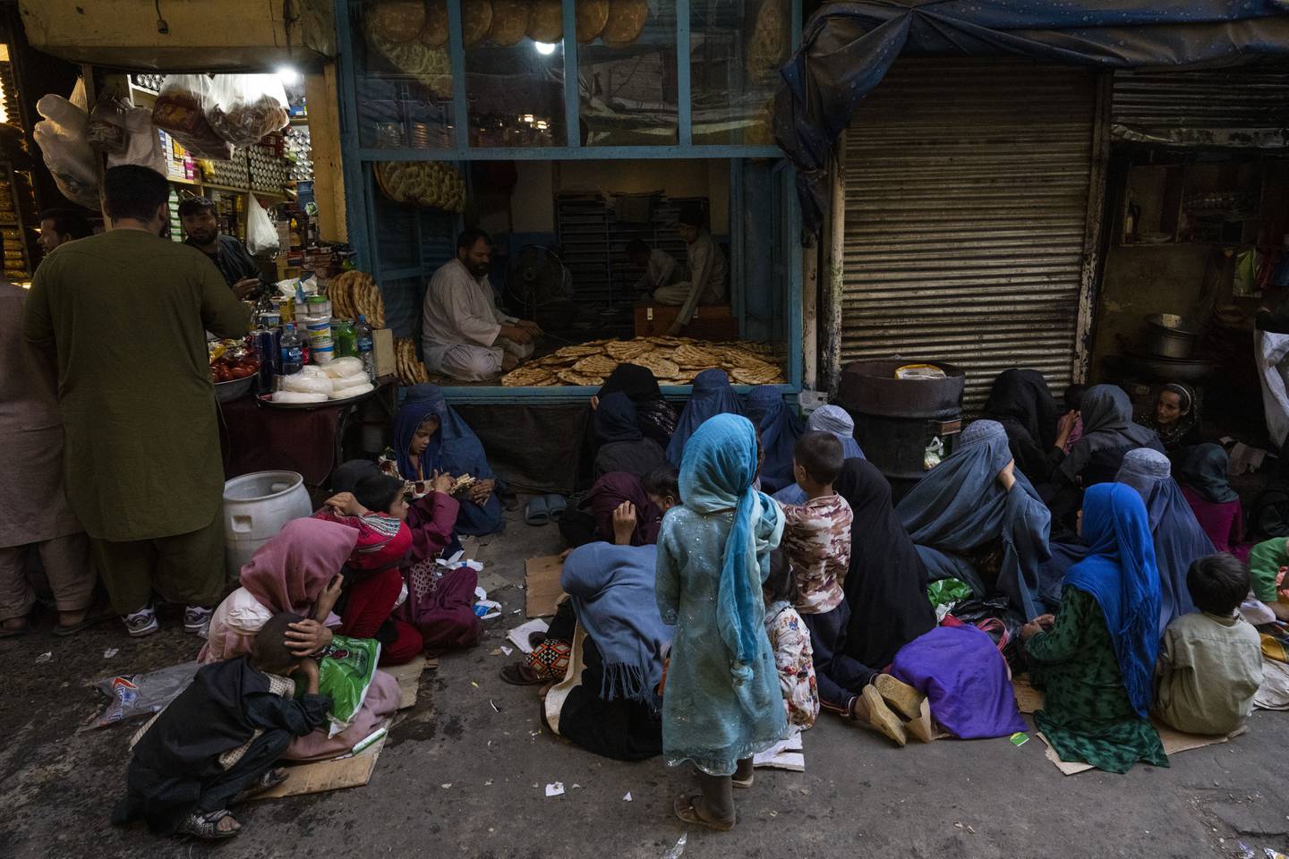 Afghanske kvinner og barn sitter utenfor et bakeri i Kabul og venter på gratis brød.