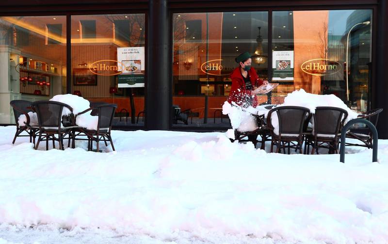 A worker cleans snow from a table outside her coffee shop after heavy snowfall in Madrid, Spain, January 11, 2021. REUTERS/Sergio Perez