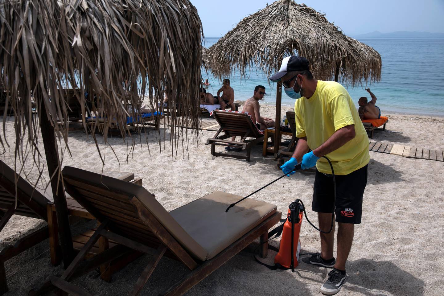 An employee disinfects sunbeds against coronavirus, at Alimos beach, near Athens, on Saturday, May 16, 2020. Greece allowed the reopening of organized beaches, where visitors pay to get in, from Saturday when a heat wave is expected to hit the country, a measure that would affect 515 beaches all over Greece, where shade umbrellas must be planted at least 4 meters (13 feet) apart, and a maximum 40 people will be allowed in every 1,000 square meters (11,000 square feet) of beach. (AP Photo/Yorgos Karahalis)