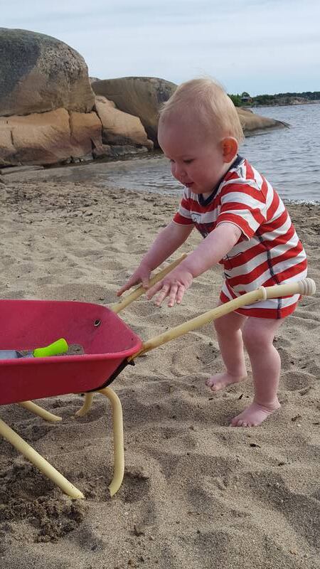 Liten gutt med trillebår på stranda.