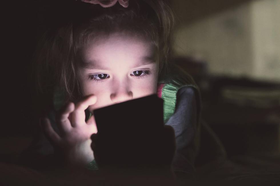 Little girl with smartphone lying in a bed, bedtime