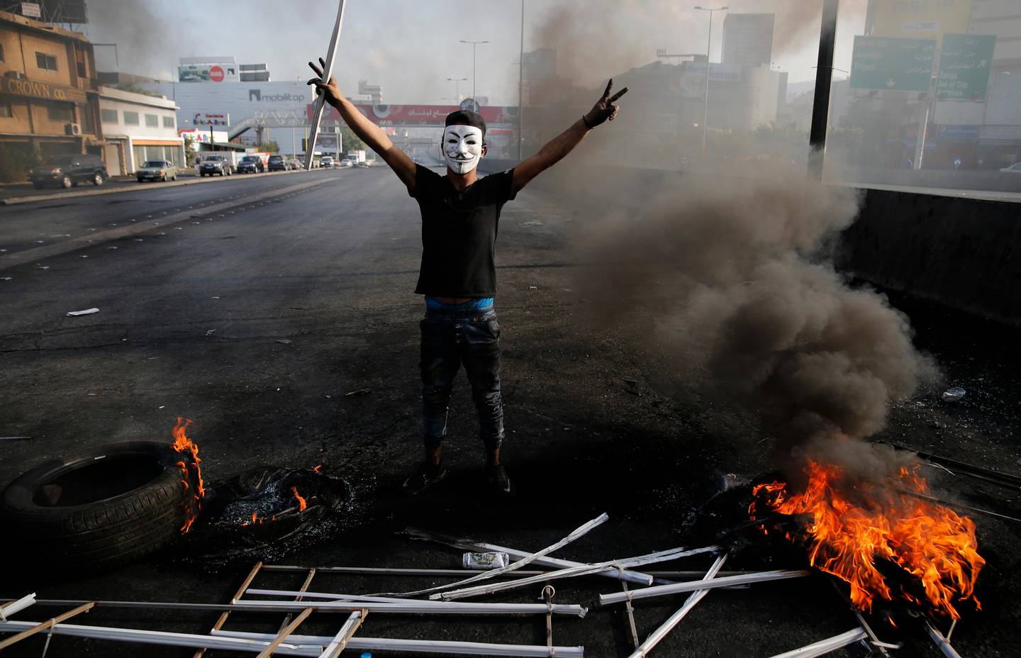 An anti-government protester flashes victory signs near burning tires as he blocks a highway that links to north Lebanon by burned tires, in east Beirut, Lebanon, Sunday, Oct. 20, 2019. Protests erupted in Lebanon after the government proposed new taxes criticized for hitting low income groups the hardest. (AP Photo/Hussein Malla)