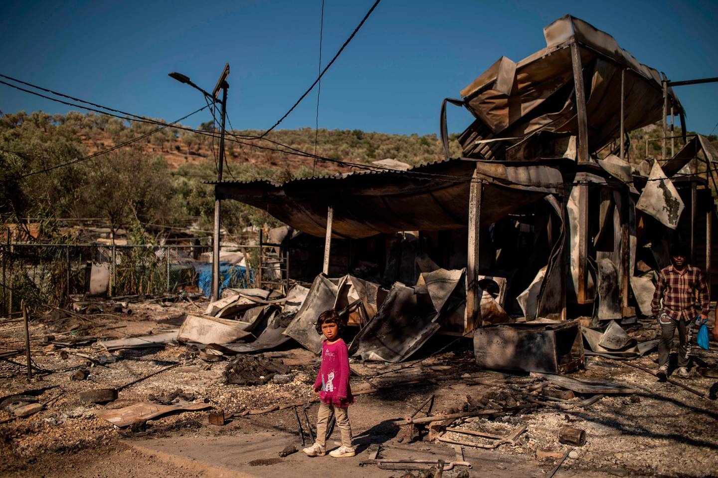 TOPSHOT - A girl stands amid rubbles in the burnt camp of Moria on the island of Lesbos after a major fire broke out, on September 9, 2020. - Thousands of asylum seekers on the Greek island of Lesbos fled for their lives on September 9, 2020 as a huge fire ripped through the camp of Moria, the country's largest and most notorious migrant facility. Over 12,000 men, women and children ran in panic out of containers and tents and into adjoining olive groves and fields as the fire destroyed most of the overcrowded, squalid camp. The blaze started just hours after the migration ministry said that 35 people had tested positive at the camp. (Photo by ANGELOS TZORTZINIS / AFP)