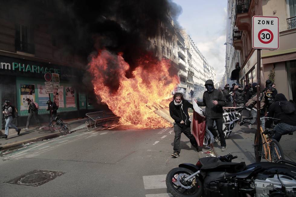 Demonstranter går forbi en søppelbrann startet under 1. mai-opptøyer i Paris, Frankrike. Foto: Lewis Joly / AP / NTB