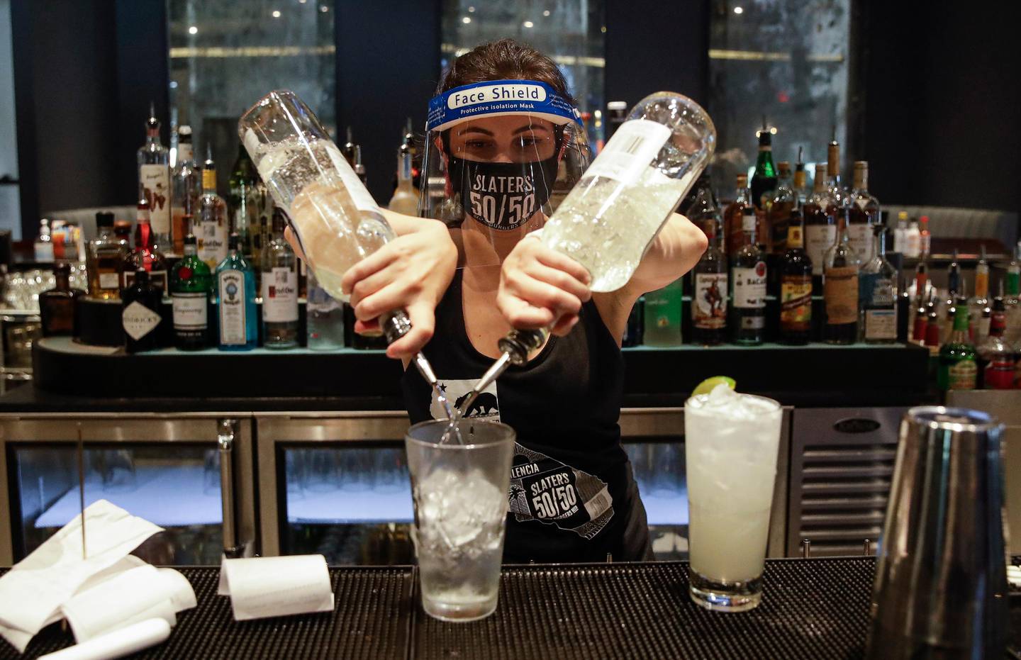 FILE - In this July 1, 2020, file photo, a bartender mixes a drink while wearing a mask and face shield at Slater's 50/50 in Santa Clarita, Calif. California Gov. Gavin Newsom on Monday, July 13, 2020, extended the closure of bars and indoor dining statewide and ordered gyms, churches and hair salons closed in most places as coronavirus cases keep rising in the nation's most populated state. (AP Photo/Marcio Jose Sanchez, File)
