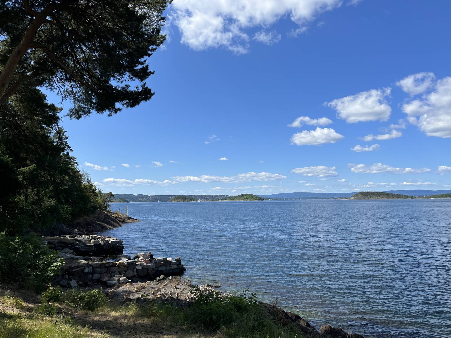 Ormøyas kommunale områder kan brukes av alle. Kommunen er i dialog med bymiljøetaten om skilting.
Et blått hav som strekker seg langt ut fra stranden, som er mer stein enn sandstrand. På et utstikkende berg sitter en jente å leser.