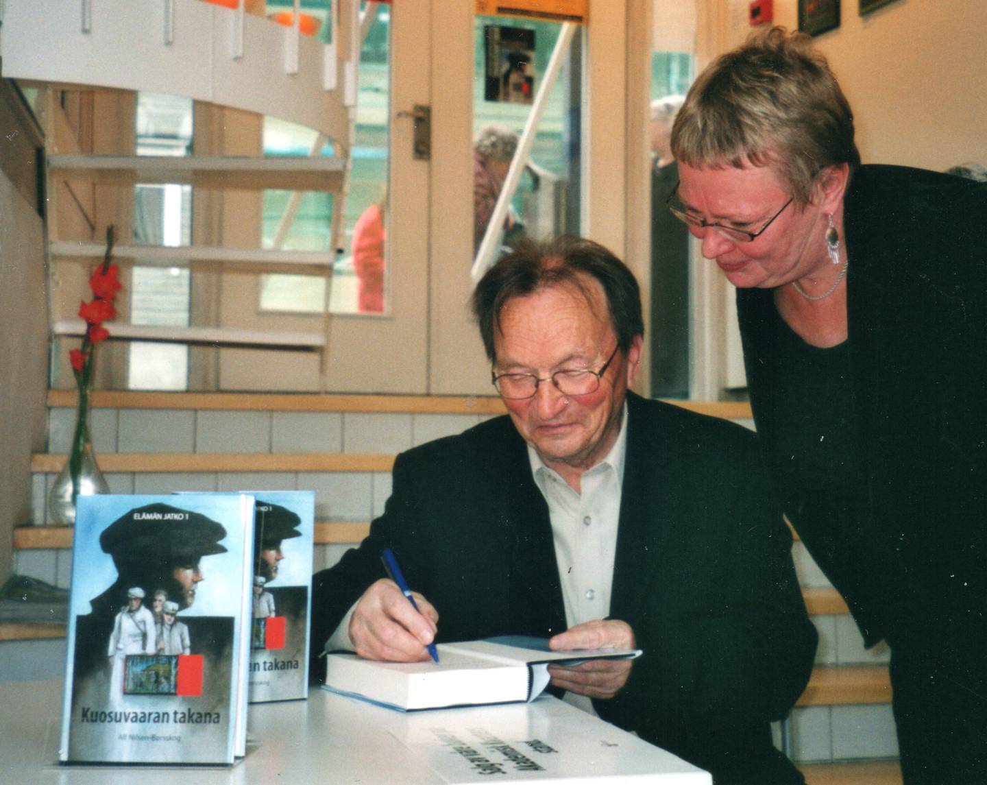 Eira Söderholm sikrer seg et signert eksemplar av Alf Nilsen-Børsskogs første roman på kvensk, i 2004. Ti år senere kom Söderholms kvenske grammatikk, bygd på blant annet Børsskogs romanserie.