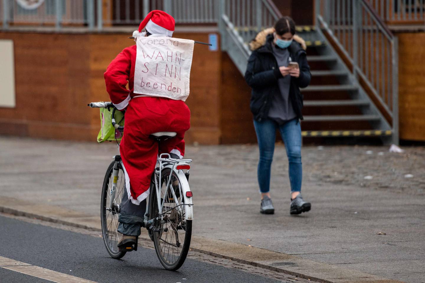 A cyclist dressed as Santa Claus drives through the city center with a poster reading "End the Corona madness" at Neumarkt in Dresden, eastern Germany on December 12, 2020. - The planned demonstration of the "Querdenken" movement protesting against measures imposed by the German government to limit the spread of the novel coronavirus COVID-19 was banned by several court orders. (Photo by STRINGER / AFP)