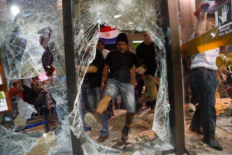 En mann sparker i et knust vindu i kongressbygningen i Paraguays hovedstad Asunción fredag. 