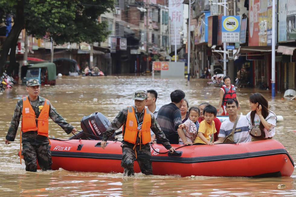Hjelpemannskaper evakuerer innbyggere fra flomvann i byen Tuojiang i Hunan-provinsen i Kina. Landet er under den verste hetebølgen på flere tiår. I juni ble også flere nedbørsrekorder slått. Foto: Jiang Linfeng/Xinhua via AP, File)