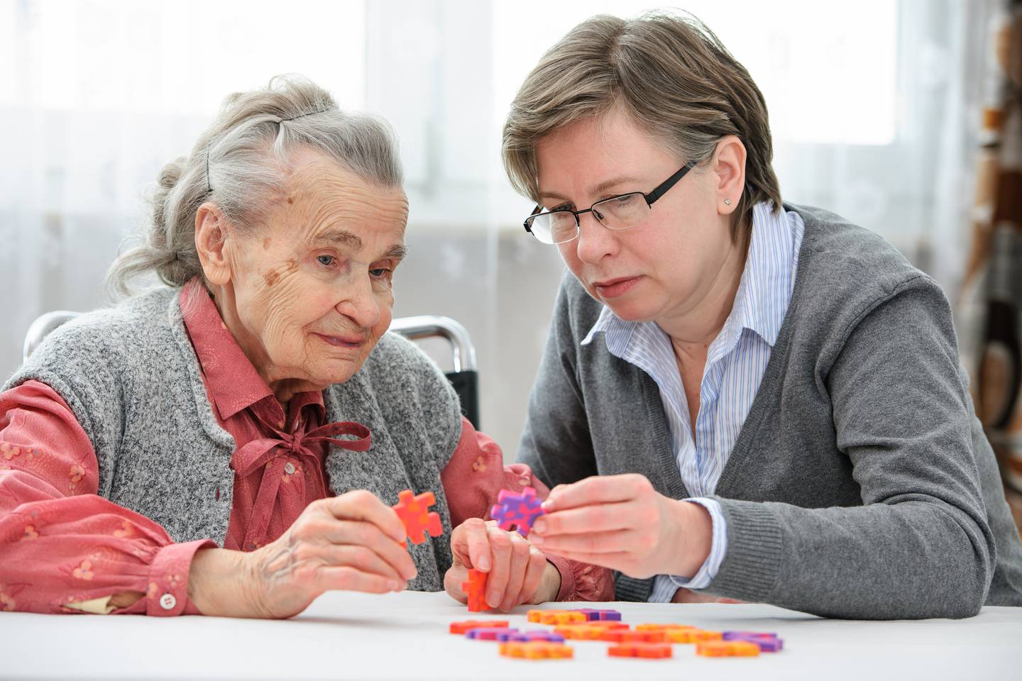 Eldrepleie som leker puslespill med eldre kvinne på sykehjem