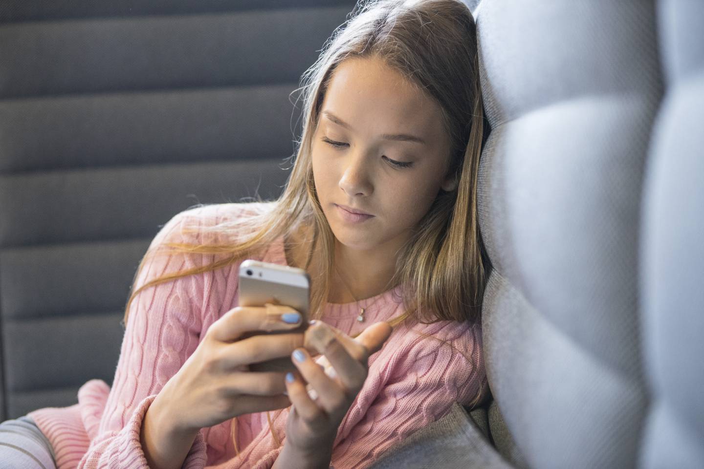 Ung jente i tenårene sitter i sofa og sjekker mobilen sin.
