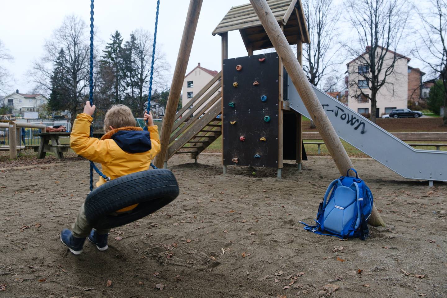 Barn med blå sekk alene på en lekeplass.