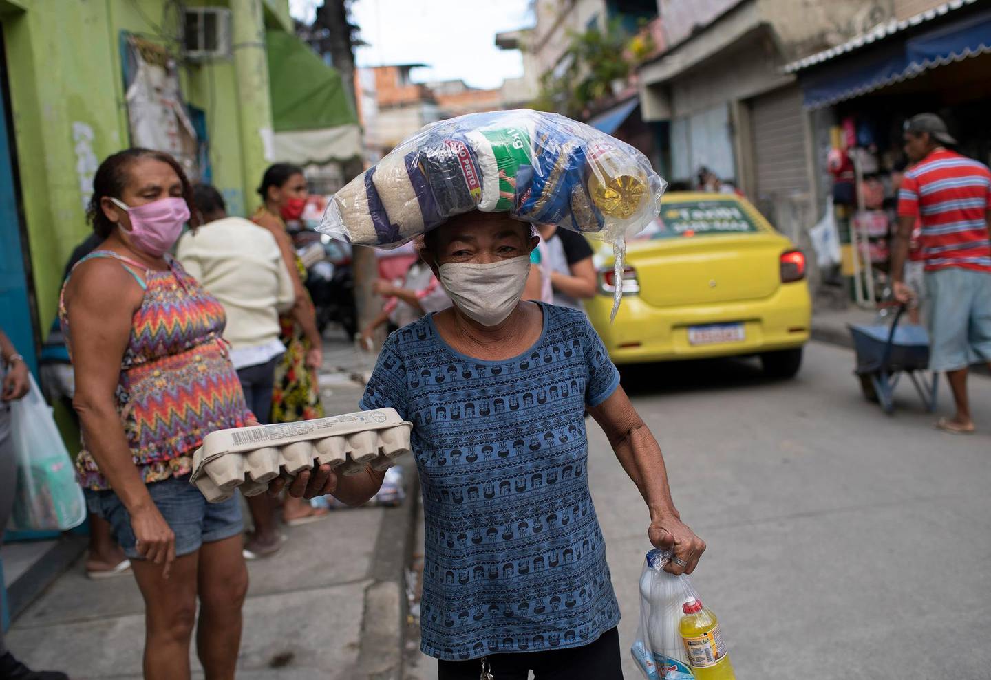 Maria Rita Dias dos Santos, 53, wearing a protective mask, carries food donated food from former inmates, part of a nonprofit organization known as  Eu sou Eu or I am me, who are delivering food to people struggling due to the new coronavirus pandemic, at the Para-Pedro favela in Rio de Janeiro, Brazil, Friday, May 8, 2020. (AP Photo/Silvia Izquierdo)