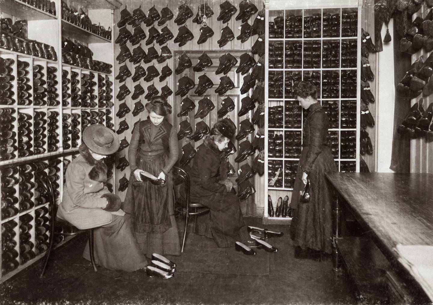 Ekspeditriser hjelper med å finne fram riktige kalosjer i butikkhylle i Gunerius Pettersen magasin i 1902.