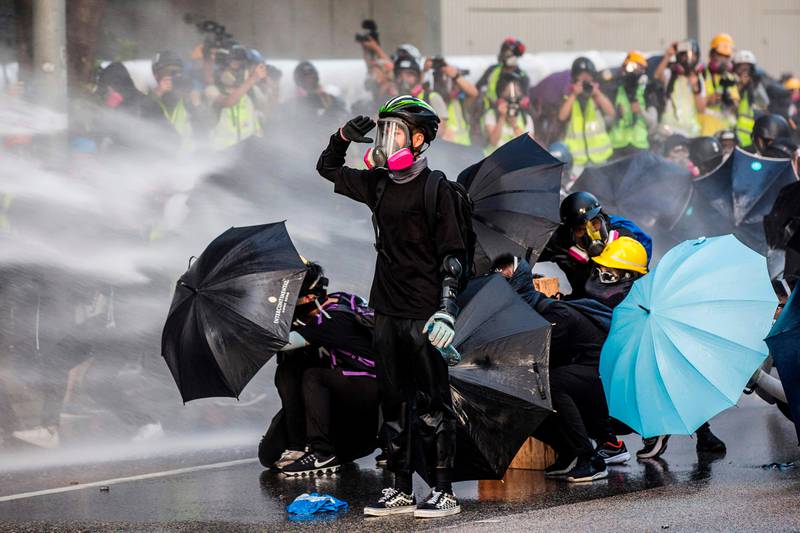 (FILES) In this file photo taken on September 15, 2019, pro-democracy protesters react as police fire water cannons outside the government headquarters in Hong Kong. - Some of them have lost their jobs, suffered life-changing injuries and even been forced into exile. But six months into Hong Kong's demonstrations, pro-democracy protesters say they aren't backing down. (Photo by ISAAC LAWRENCE / AFP) / TO GO WITH HongKong-China-politics-unrest,FOCUS by Su Xinqi and Yan Zhao
