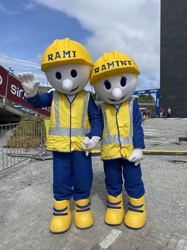 To maskoter i bygningsarbeiderklær med gul hjelm. De holder hender.