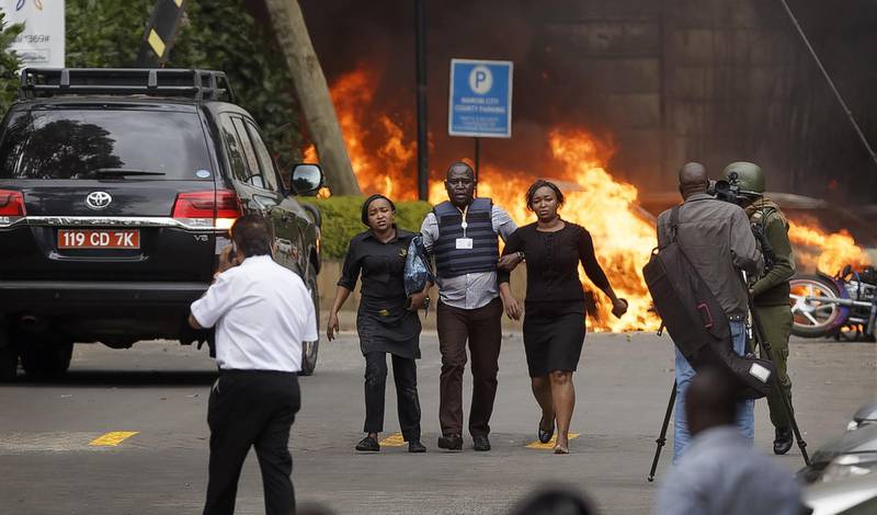 Security forces help civilians flee the scene as cars burn behind, at a hotel complex in Nairobi, Kenya Tuesday, Jan. 15, 2019. Extremists have launched an attack on a luxury hotel in Kenya's capital, sending people fleeing in panic as explosions and heavy gunfire reverberate through the neighborhood. A police officer says he saw bodies, "but there was no time to count the dead." Al-Shabab _ the Somalia-based extremist group _ is claiming responsibility. (AP Photo/Ben Curtis)