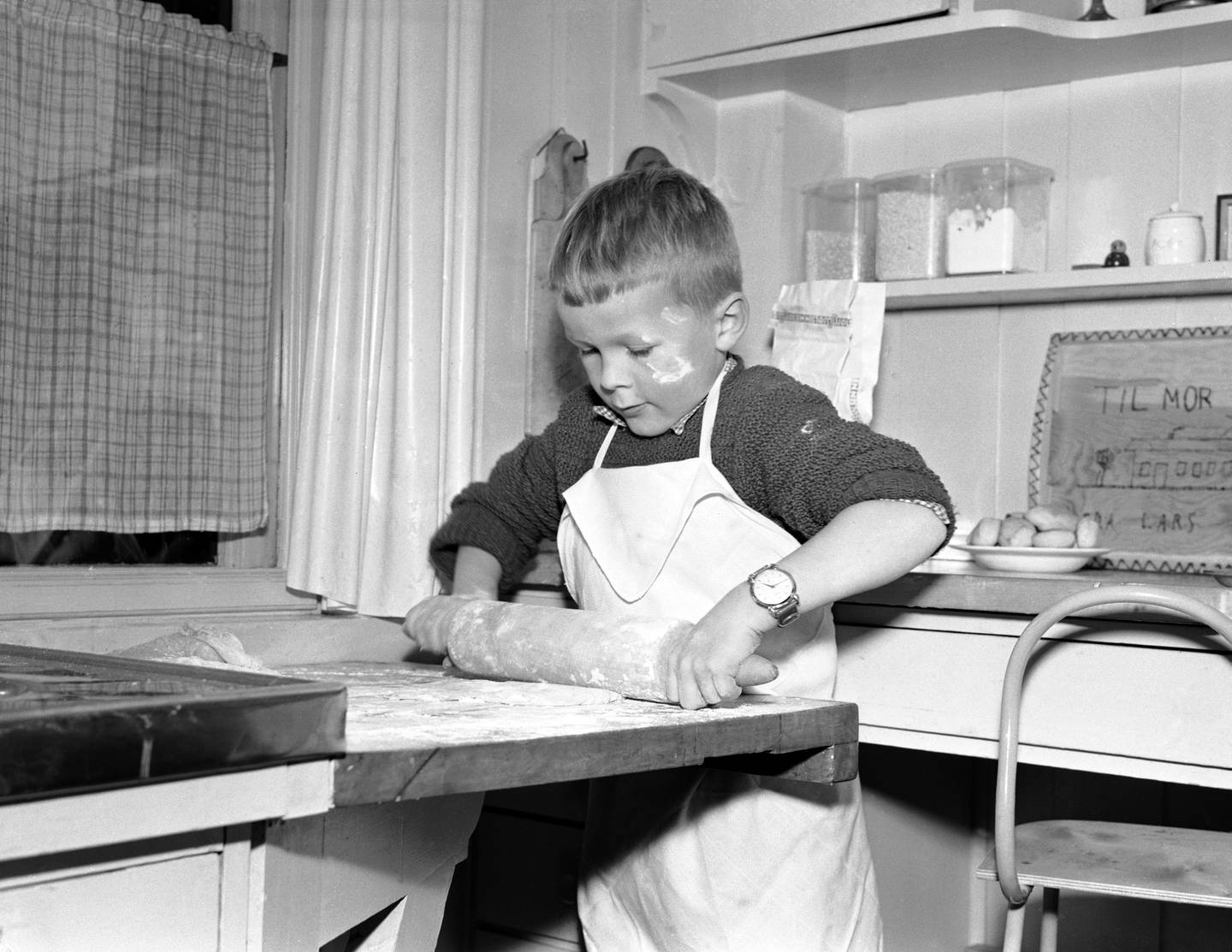 OSLO 19541028 Barn baker julekaker. Liten gutt står på kjøkkenet med forkle og kjevler kakedeig.