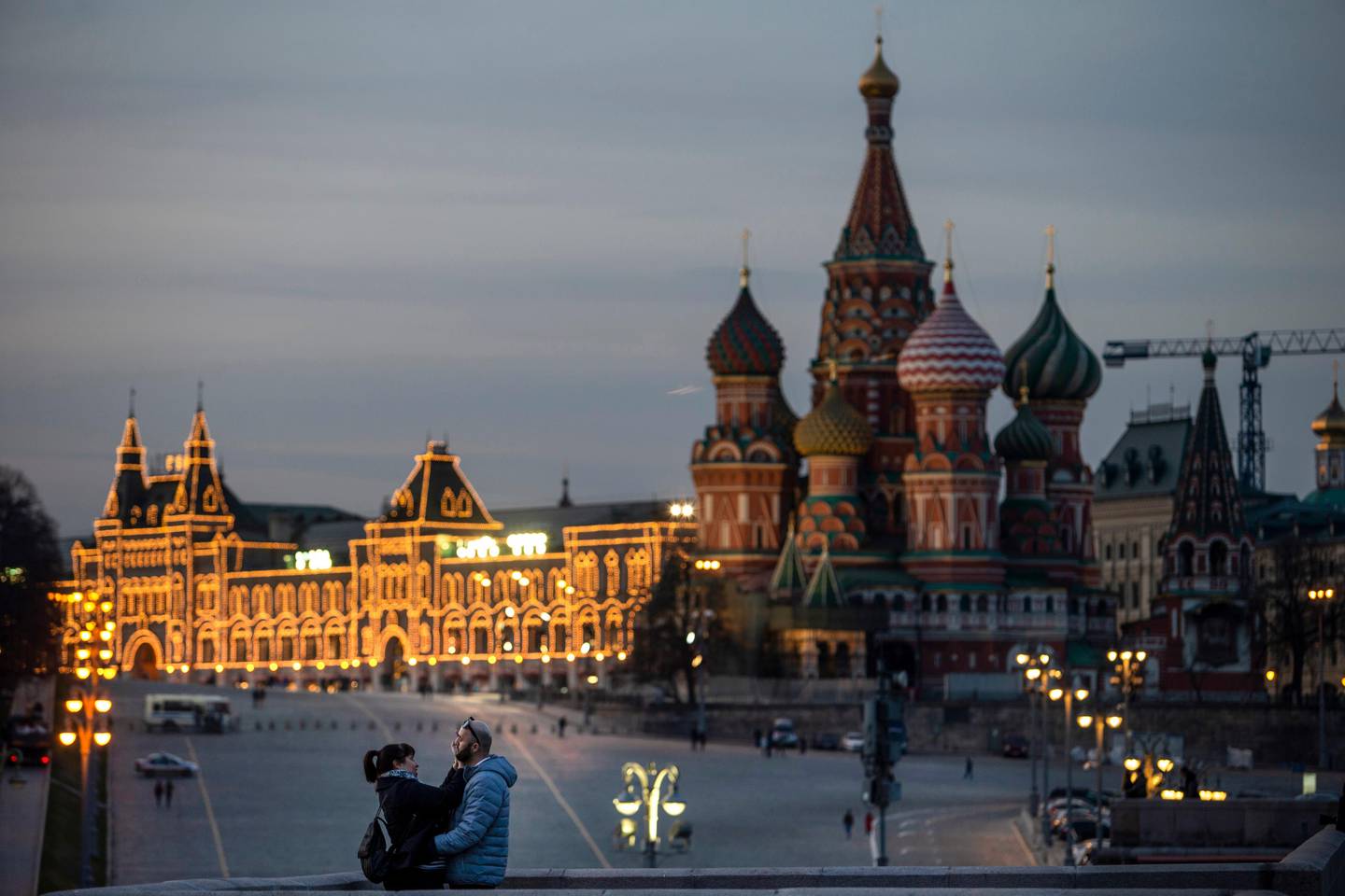 A couple enjoy warm weather on a bridge with St. Basil's Cathedral, right, and an almost empty Red Square after sunset in Moscow, Russia, on Saturday, March, 28, 2020. The new coronavirus causes mild or moderate symptoms for most people, but for some, especially older adults and people with existing health problems, it can cause more severe illness or death. (AP Photo/Alexander Zemlianichenko Jr)