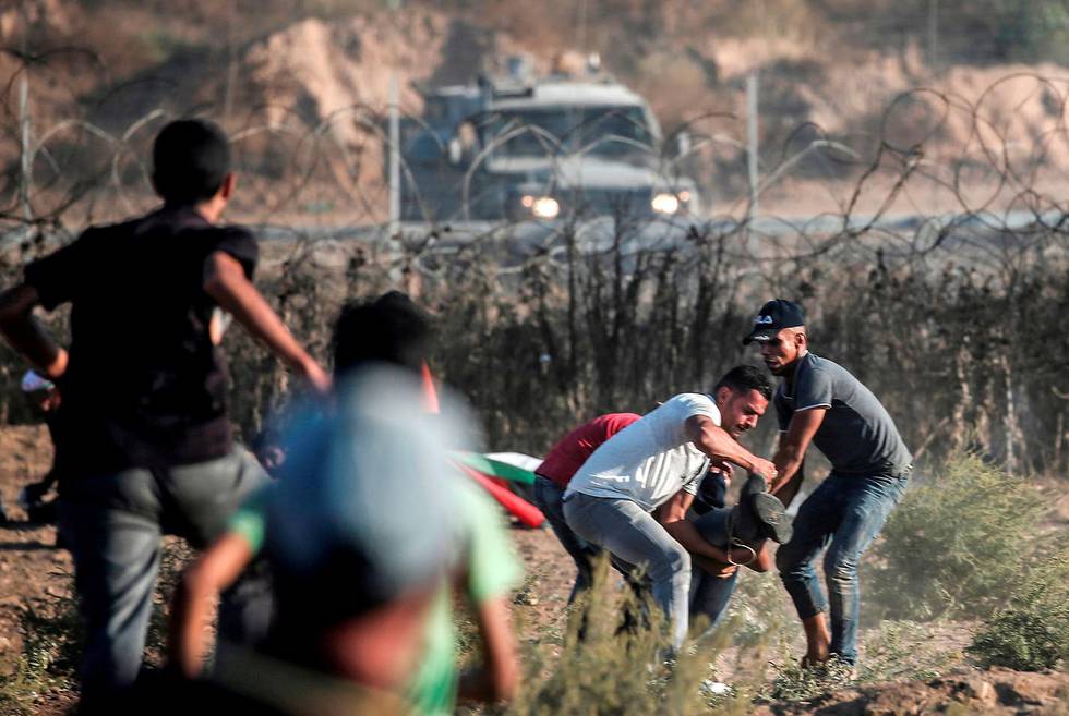 Palestinian protesters carry away an injured comrade amidst clashes with Israeli forces during a demonstration along the border with Israel east of Bureij in the central Gaza Strip on October 18, 2019. (Photo by MAHMUD HAMS / AFP)