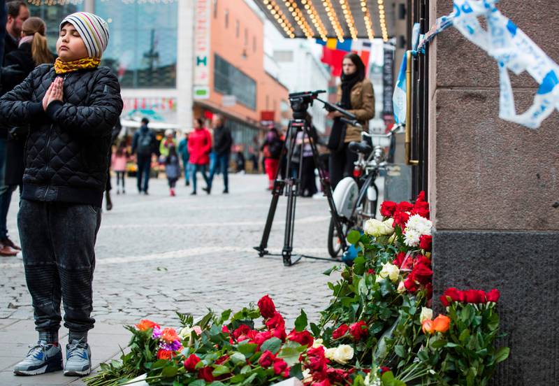 ETTER ANGREPET: En gutt stiller seg opp med hendene foran brystet etter å ha lagt ned blomster like ved stedet der angrepet i Stockholm fant sted fredag ettermiddag.
