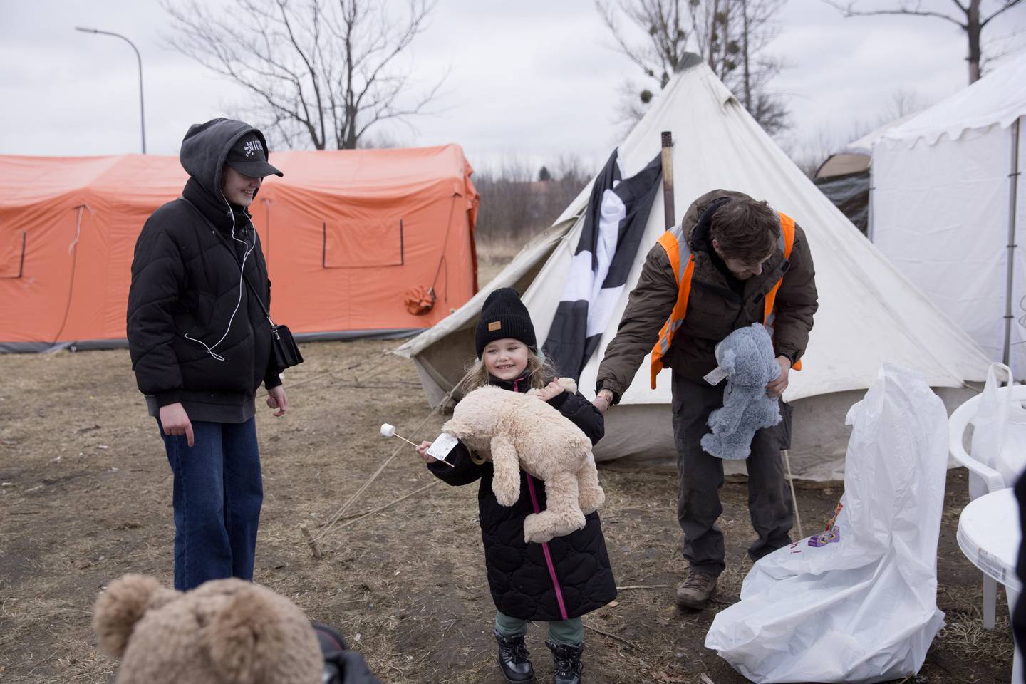 Femåringen Zlata får en bamse av en frivillig hjelpearbeider utenfor mottakssenteret i Przemysl. Storesøsteren Vika er med henne.