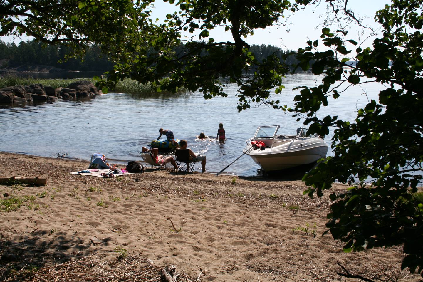 Mennesker på en strand med grønne trær i forkant og innsjøen bak.