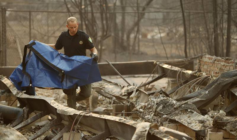 Sgt. Nathan Lyberger of the Yuba County Sheriff Department, prepares a bag to move human remains found at a burned out home at the Camp Fire, Sunday, Nov. 11, 2018, in Paradise, Calif. (AP Photo/John Locher)