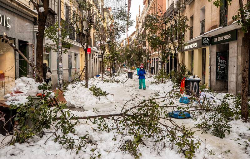 People walk along a street with snow and fallen tree branches during after a heavy snowfall in downtown Madrid, Spain, Sunday, Jan. 10, 2021. A large part of central Spain including the capital of Madrid are slowly clearing snow after the country's worst snowstorm in recent memory. (AP Photo/Manu Fernandez)