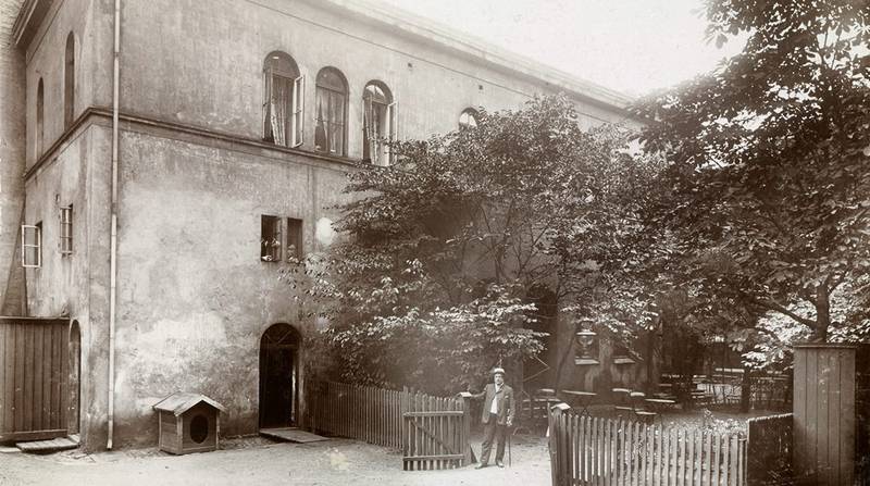 Bakgården i Rosenkrantz gate 7 fotografert før gården ble revet i 1904. Bakbygningen inneholdt opprinnelig gutteskolens gymsal. På bildet er «skolegården» tydeligvis blitt omgjort til uteservering. FOTO: NARVE SKARPMOEN/OSLO MUSEUM