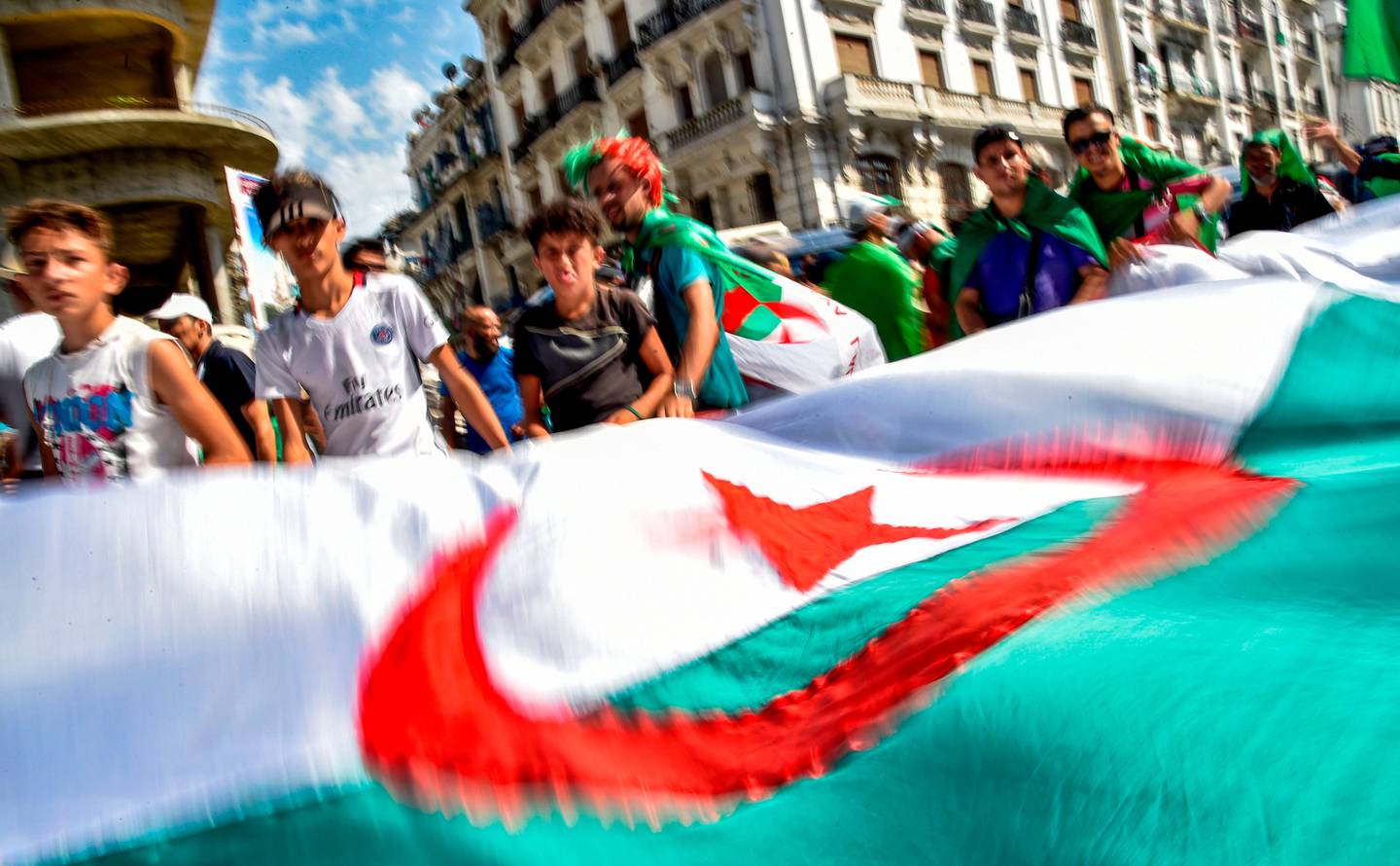 Algerian demonstrators wave a large national flag as they gather in the streets of the capital Algiers against the ruling class amid an ongoing political crisis in the country, on the 22nd consecutive Friday protest on July 19, 2019, coinciding with the Egypt 2019 Africa Cup of Nations final match between Algeria and Senegal. - In April, long-standing president Abdelaziz Bouteflika resigned after weekly Friday protests against his expected candidacy for elections, and football fans have been heavily involved in demonstrations. (Photo by RYAD KRAMDI / AFP)