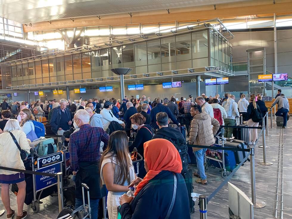 Bildet er fra Oslo lufthavn Gardermoen. Det er av folk som står i kø for å få sjekket inn bagasje. Det er teknisk trøbbel, så køene er lange. Noen folk har på munnbind. Andre er kledd for sommervær.
Foto: Heiko Junge / NTB