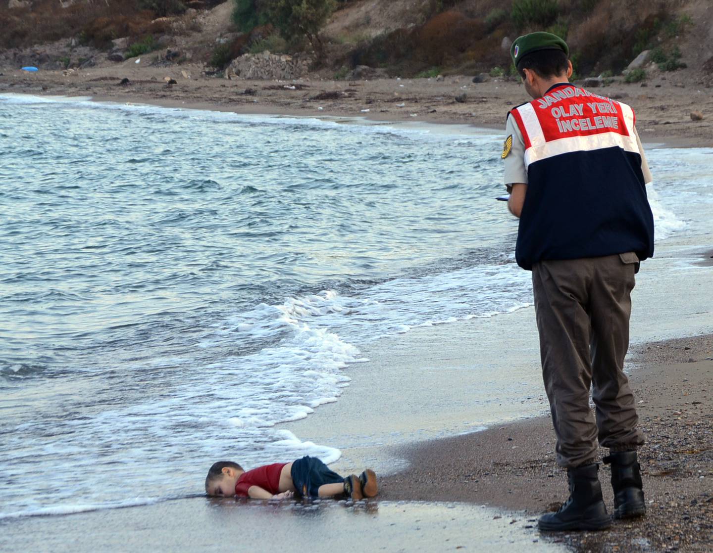ADDS IDENTIFICATION OF CHILD  A paramilitary police officer investigates the scene before carrying the lifeless body of Aylan Kurdi, 3, after a number of migrants died and a smaller number were reported missing after boats carrying them to the Greek island of Kos capsized, near the Turkish resort of Bodrum early Wednesday, Sept. 2, 2015. The family ó Abdullah, his wife Rehan and their two boys, 3-year-old Aylan and 5-year-old Galip ó embarked on the perilous boat journey only after their bid to move to Canada was rejected. The tides also washed up the bodies of Rehan and Galip on Turkey's Bodrum peninsula Wednesday, Abdullah survived the tragedy. (AP Photo/DHA) TURKEY OUT  ONLINE OUT