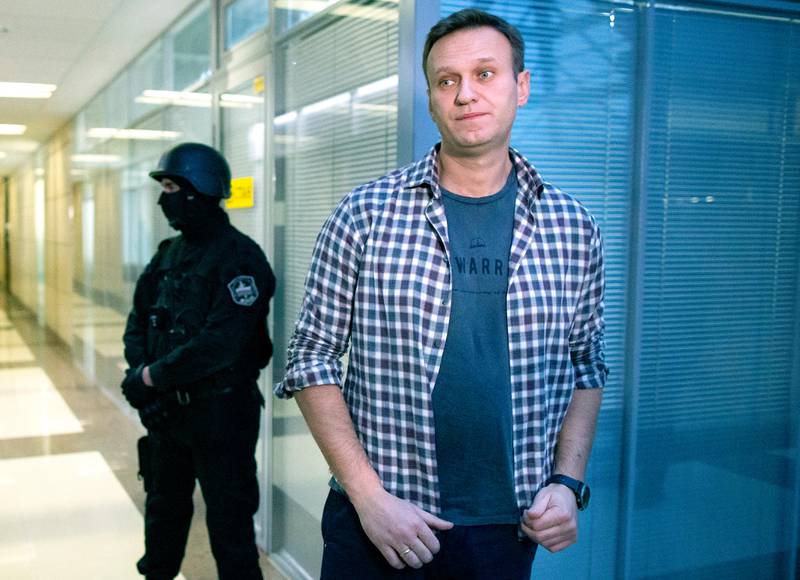 FILE - In this Dec. 26, 2019 file photo, Russian opposition leader Alexei Navalny speaks to the media in front of a security officer standing guard at the Foundation for Fighting Corruption office in Moscow, Russia. Navalny was jailed soon after arriving to Moscow after authorities accused him of violating of the terms of his 2014 fraud conviction. A court on Thursday Jan. 28, 2021, is to hear an appeal on the ruling to remand him into custody. Next week, another court will decide whether to send him to prison for several years for the alleged violations. (AP Photo/Alexander Zemlianichenko, File)