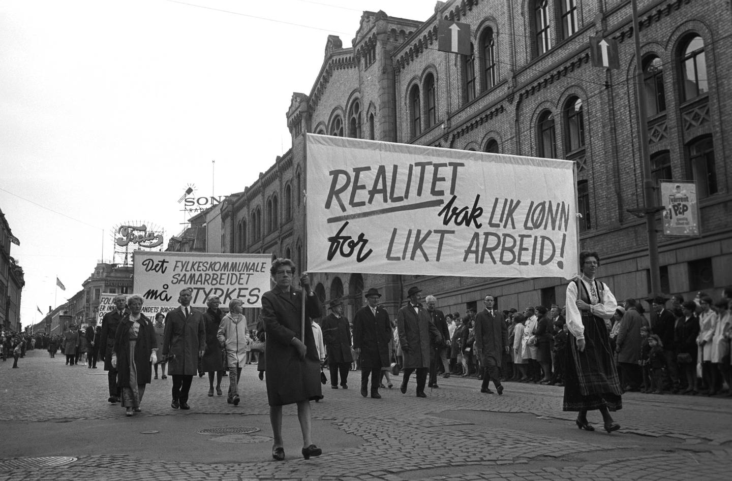 Første mai demonstrasjoner i Oslo i 1968. Her passerer første mai toget Stortinget på vei ned Karl Johans gate. Plakater med slagord om Lik lønn for likt arbeid.