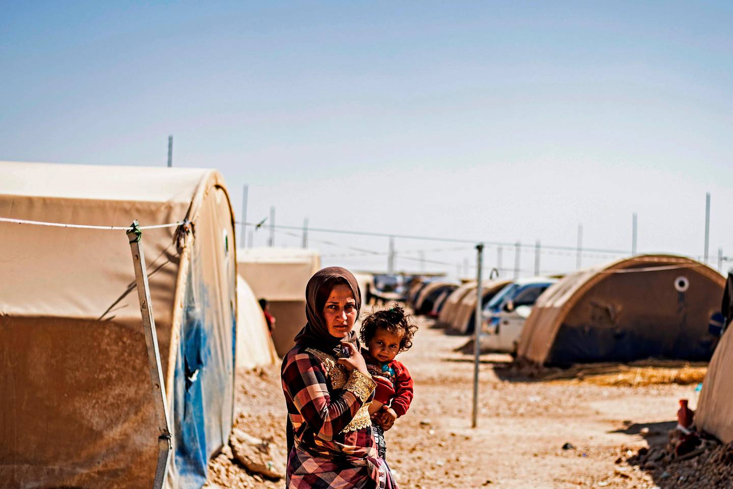 A woman stands carrying a child at the Washukanni camp for the internally displaced near the town of Tuwaynah, west of Syria's northeastern city of Hasakah on October 8, 2020. - Tens of thousands of people were forced out of their homes and into informal settlements in Kurdish-controlled regions south of Syria's border with Turkey. Their homes and belonging have been seized or looted in the year since the Turkish offensive in October 2019 that saw Ankara capture a 120-kilometre (70-mile) long strip along its southern border. (Photo by Delil SOULEIMAN / AFP)