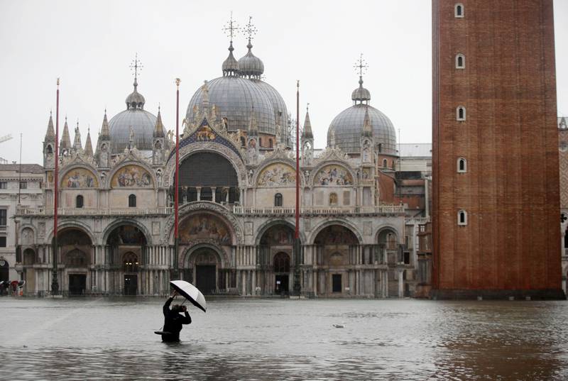 A photographer takes pictures in a flooded St. Mark's Square, in Venice, Italy, Tuesday, Nov. 12, 2019. The high tide reached a peak of 127cm (4.1ft) at 10:35am while an even higher level of 140cm(4.6ft) was predicted for later Tuesday evening. (AP Photo/Luca Bruno)