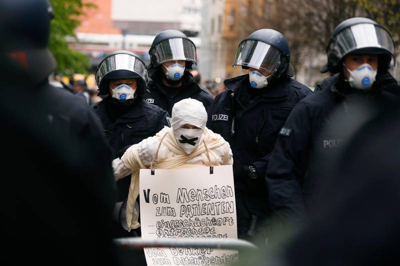 Police officers detain a person with bandages around the face, during an illegal demonstration against restrictions and measures to prevent the spread of coronavirus in Berlin, Germany, Saturday, April 25, 2020. The poster reads, "Intimidated disenfranchised remote controlled from thinker to a data donor." (AP Photo/Markus Schreiber)
