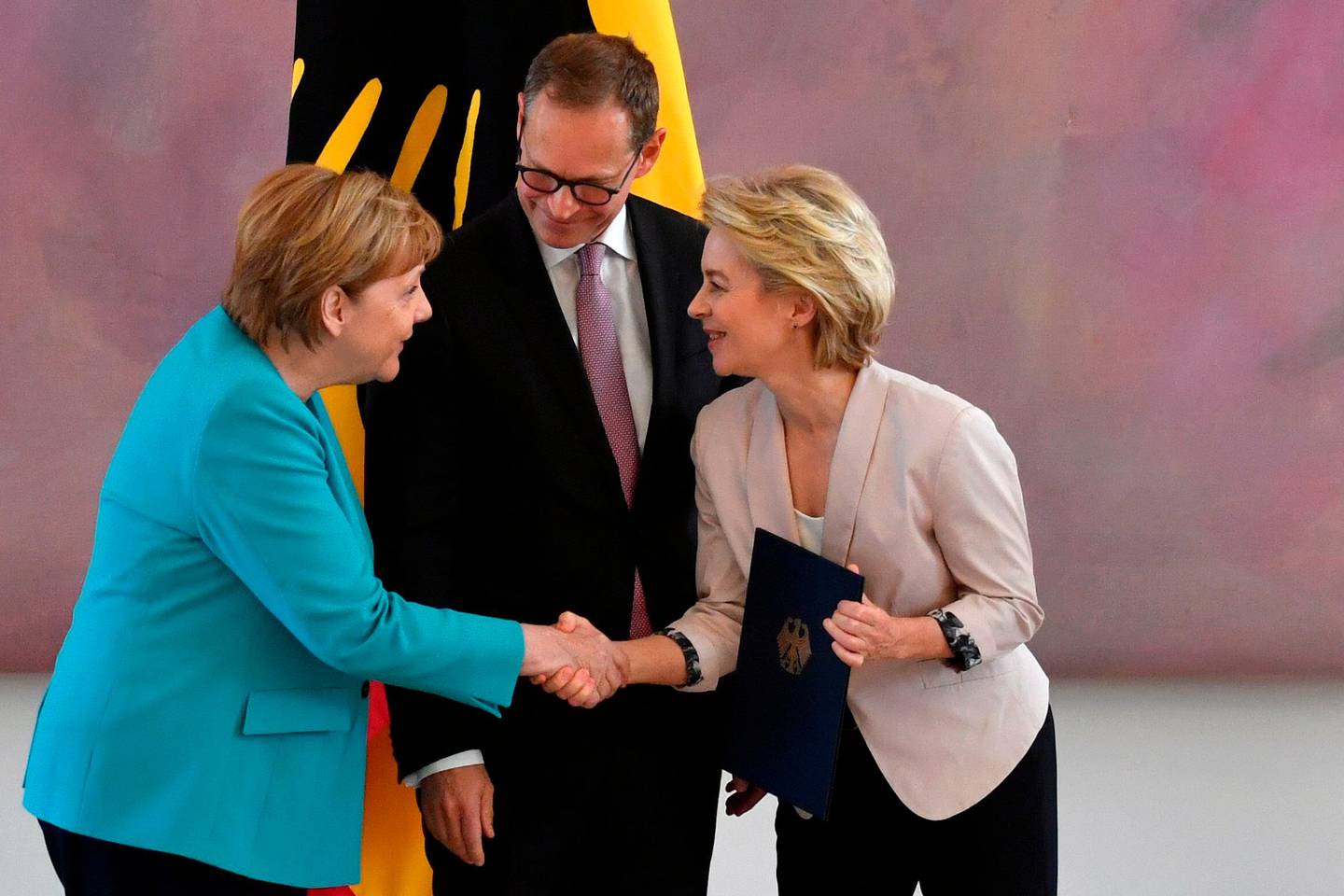 German Chancellor Angela Merkel (L) shakes hands with outgoing minister Ursula von der Leyen (R) as the vice-president of the Bundesrat (upper house of parliament) Michael Mueller watches during a handover ceremony on July 17, 2019 at Bellevue Castle in Berlin. - The leader of the CDU party Minister Annegret Kramp-Karrenbauer replaces newly elected European Commission President Von der Leyen. (Photo by John MACDOUGALL / AFP)