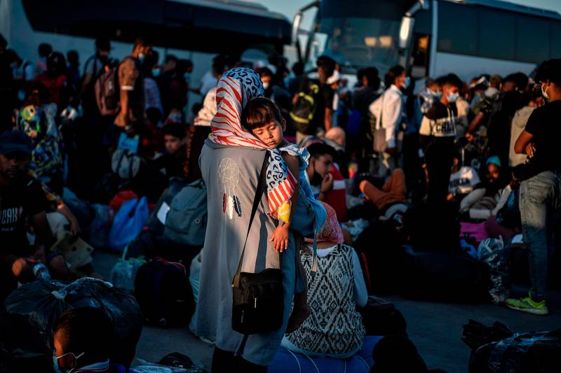 A woman holds her child as refugees from the islands of  Lesbos, Chios, Samos , Kos and Leros wait to board buses  after disembarking at the port of Lavrio, some 70 km south-east of Athens, prior to be transferred to camps in mainland Greece, on September 29, 2020. - The first groups of 724 refugees from the gutted Moria camp and another 210 from the camps at other Aegean islands were transferred on September 29, 2020, in a bid to decongest the overcrowded island camps. (Photo by LOUISA GOULIAMAKI / AFP)