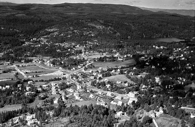 juli 1963: Stordammen ligger majestetisk til på høyden over sentrum av Konnerud, og vi skimter skolen i enden av dammen. Midt i bildet ser vi Hellingsenteret, som vi i dag kjenner som Jarlsbergsenteret. Veien som gjør en sving og fortsetter til høyre mot nedre bildekant er den nåværende Bernåsbakken, men som den gang var en del av Konne­rud­gata som hovedfartsåren ned til Konnerud. Kirken ligger fritt til opp fra Stubberudveien, og vi ser også Poppegården på nedsiden av kirken.